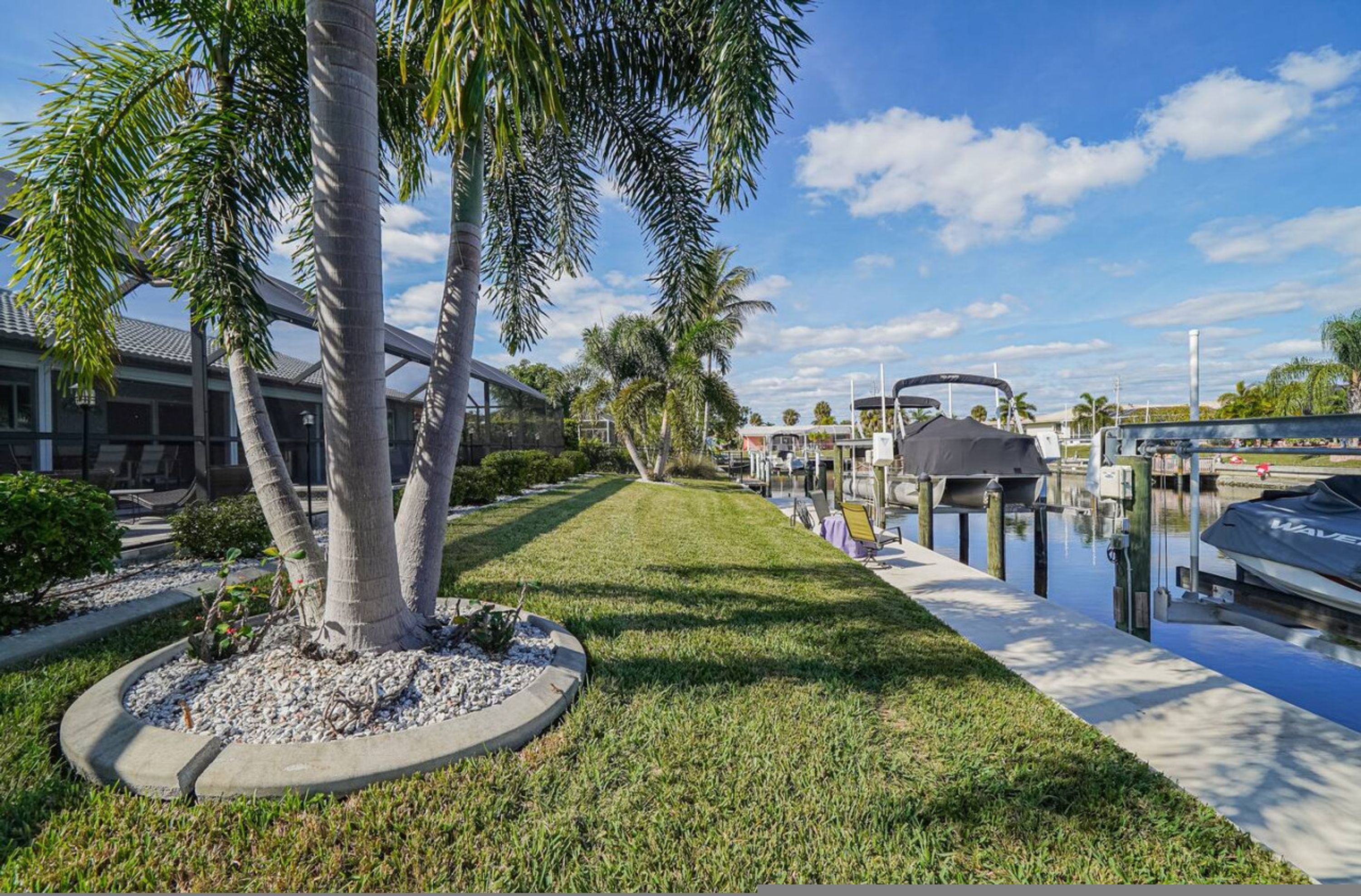 A waterfront property with a grassy pathway, palm trees, and a dock with a boat.