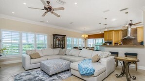 A spacious living room with a large sectional sofa, a patterned ottoman, and a ceiling fan. - Dog Friendly Walk to Fishermen s Village Pool (Punta Gorda)