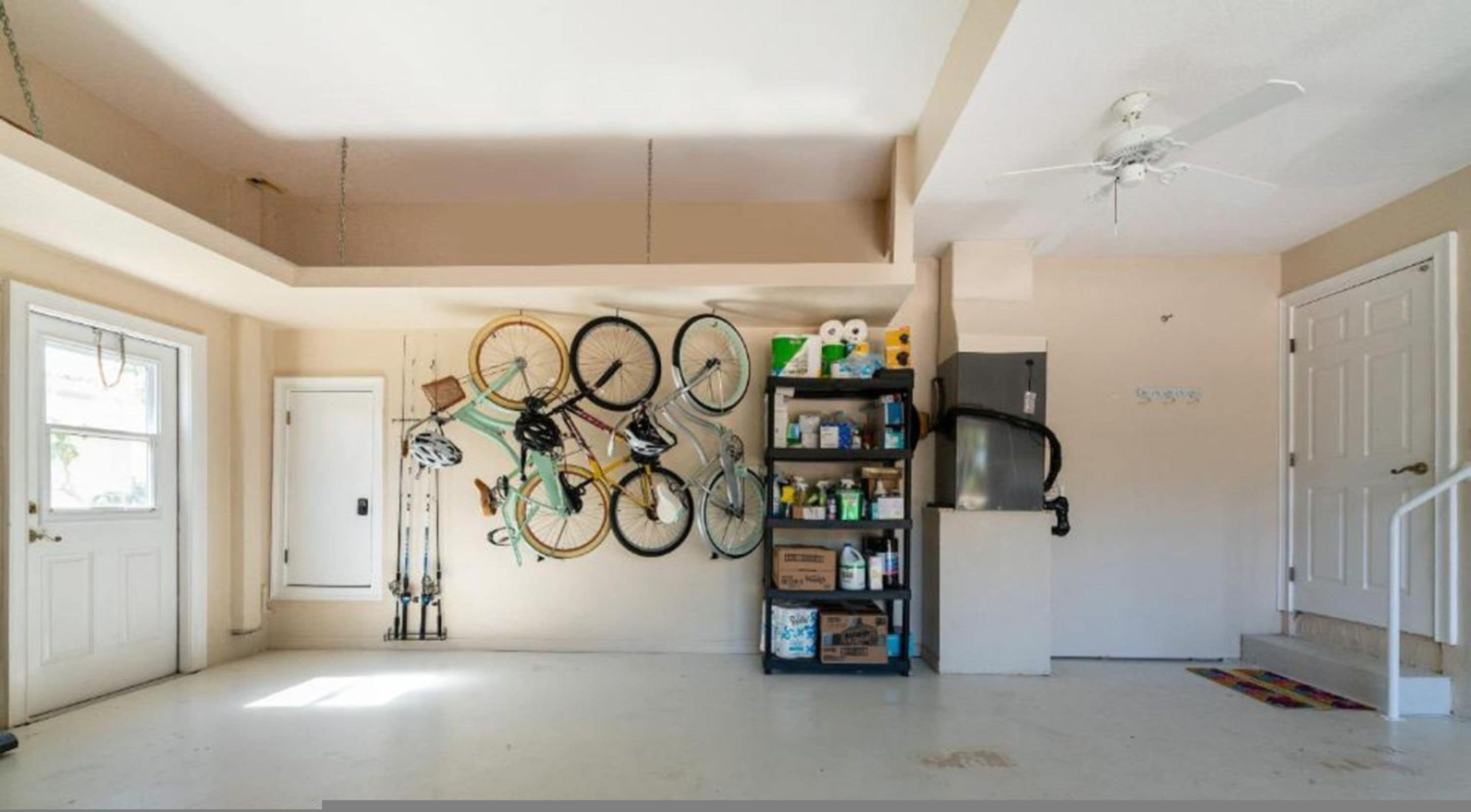 A spacious room with a ceiling fan, a wall-mounted bicycle rack, and a storage unit with various items.