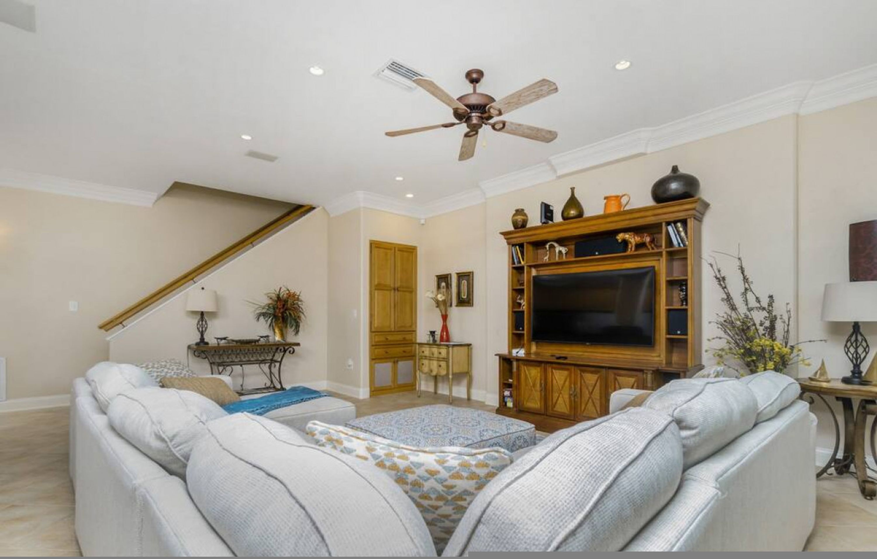 A spacious living room with a large sofa, a television, and a ceiling fan.