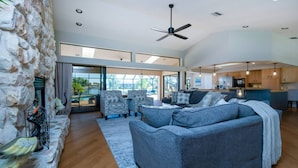A spacious living area with a stone accent wall, a large gray sofa, and a ceiling fan. - Villa Tropical Waterfront Luxury Retreat Panoramic Water Views Pool Spa (Punta Gorda)