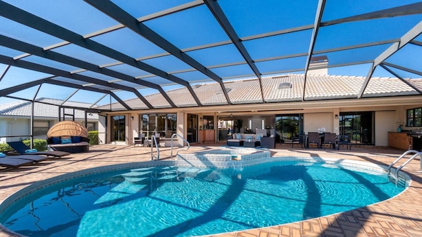 A covered outdoor swimming pool with a patio area, lounge chairs, and a seating area with a table and chairs. - Villa Tropical Waterfront Luxury Retreat Panoramic Water Views Pool Spa (Punta Gorda)