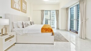 A modern bedroom with a large bed, a bedside table, and a view of a cityscape through large windows. - Lux BnB I Executive Tower I Business Bay (Dubai)