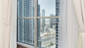 A cityscape through a window with blinds, featuring high-rise buildings and a clear sky. - Lux BnB I Executive Tower I Business Bay (Dubai)
