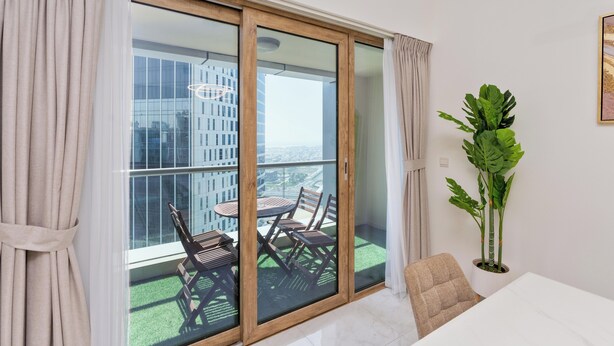A balcony with a glass door, a table, chairs, and a potted plant. - Lux BnB I Executive Tower I Business Bay (Dubai)