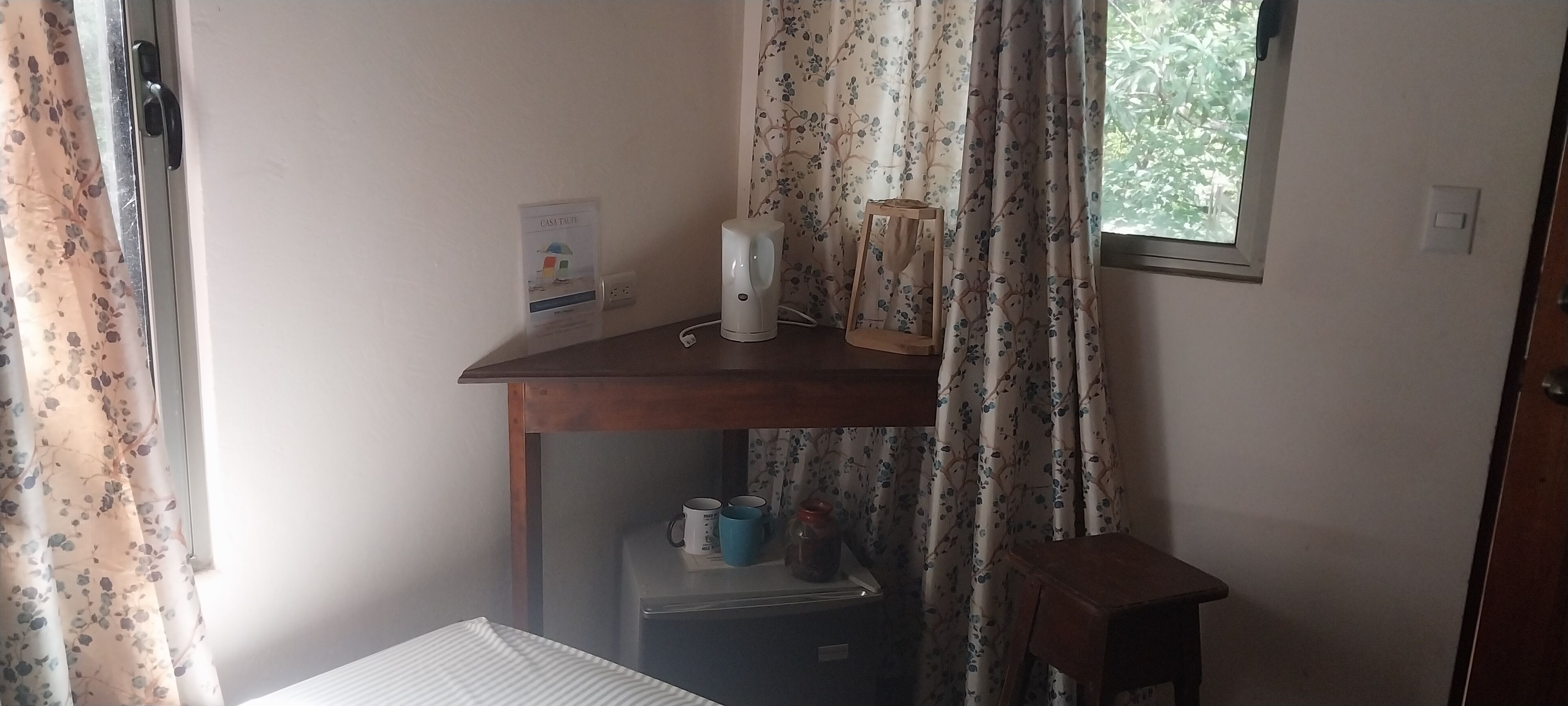 A small room with a wooden desk, a kettle, a framed picture, and a small refrigerator.