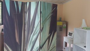 Una habitación con un ventanal grande, un dispensador de agua, un microondas y un estante blanco con un objeto verde.