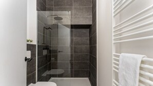 A modern bathroom with a glass-enclosed shower, a toilet, and a towel rack.