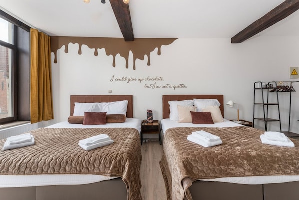 A hotel room with two beds, a wall with a chocolate drip design, and a quote saying "I could give up chocolate, but I'm not a quitter."