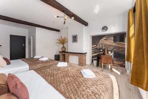 A hotel room with two beds, a fireplace, a desk, and a large window.