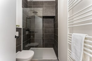 Un baño moderno con ducha de vidrio, inodoro y perchero para toallas.