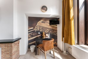 A cozy room with a fireplace, a desk with a chair, a television mounted on the wall, and a window with curtains.