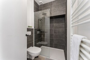 A modern bathroom with a glass-enclosed shower, a white toilet, and a white bathtub.