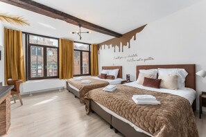 A hotel room with two beds, a window with curtains, a radiator, and a wall with a chocolate drip design.