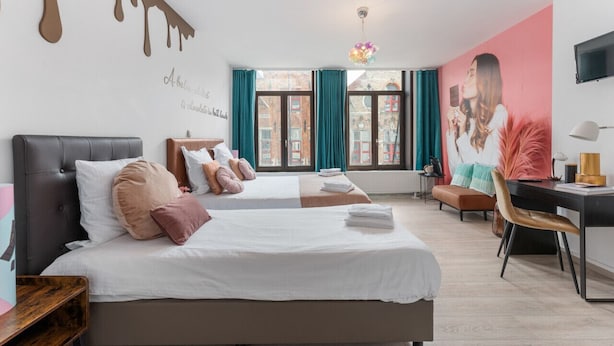 A hotel room with two beds, a desk, a chair, a TV, and a window with curtains. - Sweet chocolate room by  Charlie's choco factory - Perfect for up to 3 people! (Brugge)