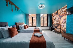 Een hotelkamer met twee bedden, een groot raam, een wanddecoratie van koekjes en een plafondventilator.