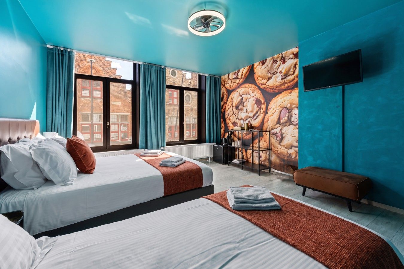 Une chambre d’hôtel moderne avec deux lits, une grande fenêtre, un téléviseur fixé au mur et une vue sur la ville.