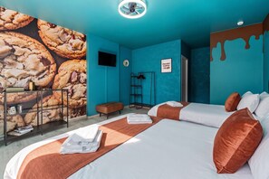 Een hotelkamer met twee bedden, een muurschildering van koekjes, een flatscreen televisie, een ladder en een bordje met de tekst 'Chocoladekoekjes'.