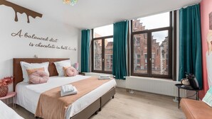 A modern bedroom with a large bed, teal curtains, a city view, and a wall quote. - Sweet chocolate room by  Charlie's choco factory - Perfect for up to 3 people! (Brugge)