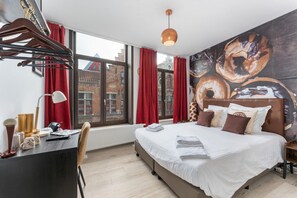 Een moderne hotelkamer met een groot bed, een bureau met een lamp en een stadszicht door grote ramen.