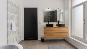 Um banheiro moderno com porta preta, radiador branco, toucador de madeira, espelho e uma janela grande.