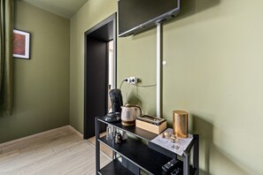 Une chambre d’hôtel avec une console noire, une machine à café, une bouilloire, une télécommande et un tableau encadré au mur.