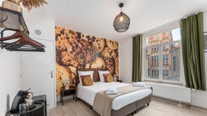Quarto com cama, cafeteira, janela com cortinas e parede com mural de biscoitos.