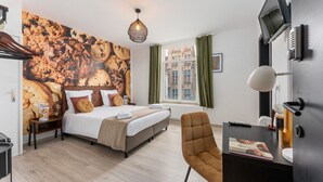 Quarto de hotel moderno com uma cama grande, uma escrivaninha com computador, uma cadeira e vista para edifícios pela janela.