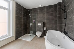 Une salle de bain moderne avec une douche à l’italienne, des toilettes et une baignoire.