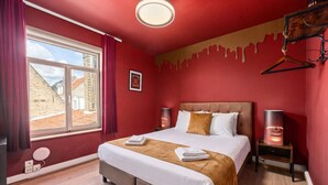 Een hotelkamer met een groot bed, twee nachtkastjes, een raam met gordijnen en uitzicht op gebouwen.