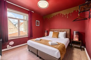 A hotel room with a large bed, two bedside tables, a window with curtains, and a view of buildings outside. - The Hot Chocolate Room by Charlie`s Choco Factory (Brugge)
