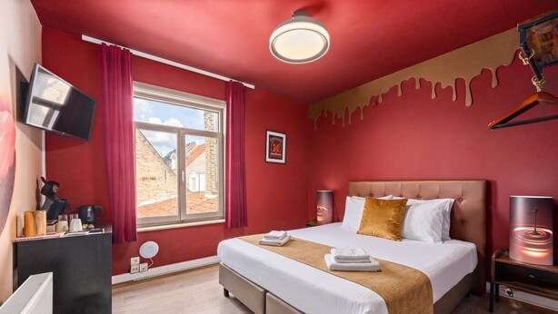 Hotelkamer met een bed, nachtlampjes, een televisie, een raam met gordijnen en uitzicht op gebouwen.