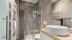 Een moderne badkamer met een douche met glazen wand, een wit wastafelmeubel en een toilet.