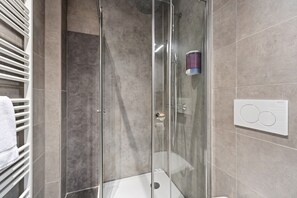 Un baño moderno con ducha envuelta en vidrio, un perchero blanco y un panel de control montado en la pared.