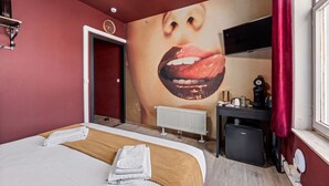 Een hotelkamer met een bed, een grote muurschildering, een bureau met een computer en een radiator.