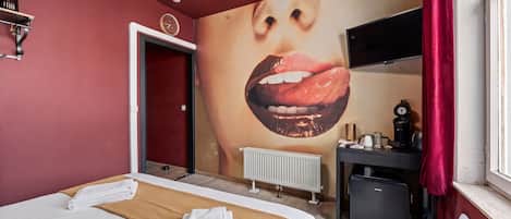 Una habitación de hotel con cama, un mural grande en la pared, un escritorio con computadora y un radiador.