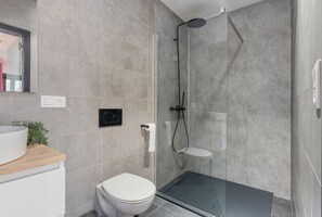Un baño moderno con cabina de ducha de vidrio, inodoro y lavamanos con encimera de madera.