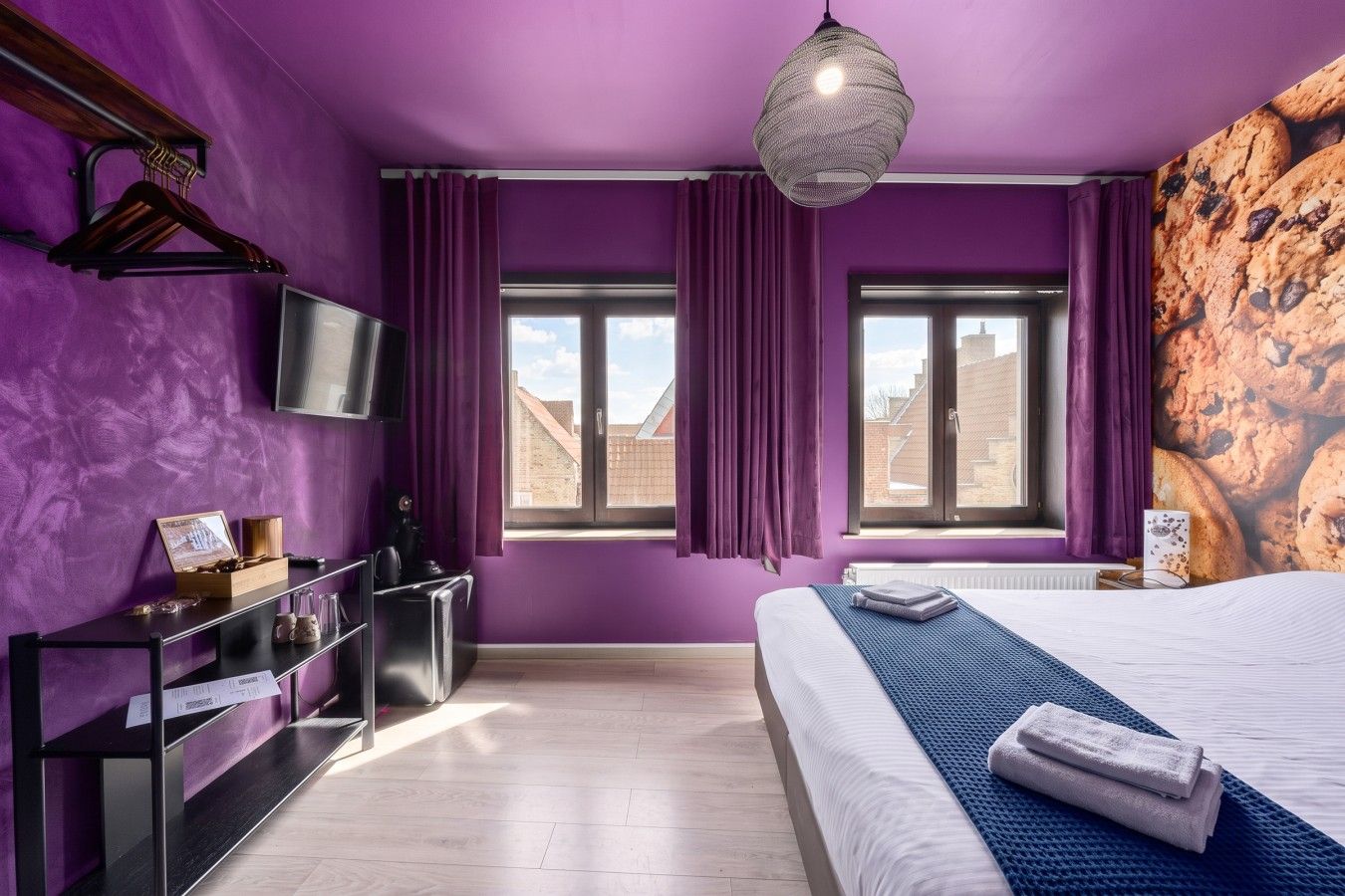 Een slaapkamer met een bed, een dressoir, een televisie en een raam met gordijnen.