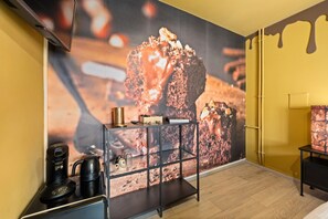Een moderne kamer met een grote muurschildering met chocoladethema, een zwarte console tafel met een koffieapparaat, en een minimalistisch design.