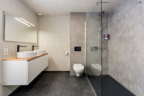 Een moderne badkamer met een douchecabine, een wit toilet en een wastafelmeubel met twee wastafels.