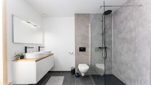 Un baño moderno con ducha de vidrio, lavamanos blanco y retrete.
