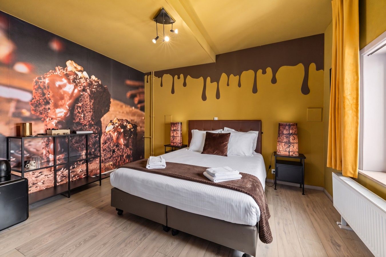 Une chambre d’hôtel avec un grand lit, des tables de chevet, une fresque murale et une fenêtre avec des rideaux.