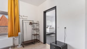 Una habitación moderna con un radiador, un calefactor independiente, un armario negro, una estantería metálica y una cortina amarilla.