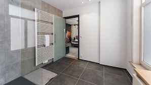 Un baño moderno con cabina de ducha de vidrio, toallero blanco y suelo de baldosas oscuras.