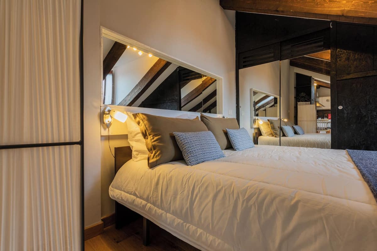 Een moderne slaapkamer met een groot bed, een hoofdeinde met geïntegreerde verlichting en een spiegel die de kamer weerspiegelt.