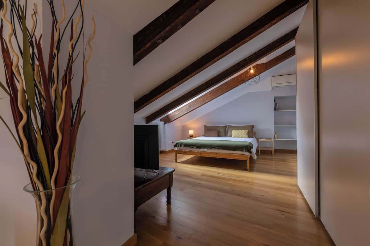Een slaapkamer met een schuine kap, een bed, nachtkastje, lamp en televisie.