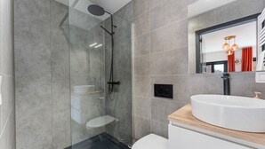 Un baño moderno con ducha envuelta en vidrio, inodoro blanco y un lavabo redondo grande con encimera de madera.