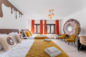 A hotel room with two beds, a large window with orange curtains, a wall art of a donut, and a large donut decoration on the wall.