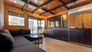 A modern interior with a black sofa, a round glass table, and a kitchen area with wooden paneling and a built-in stove.