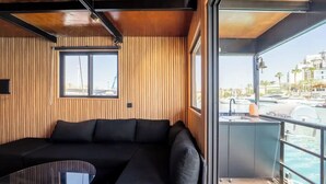 A modern room with a black sectional sofa, a glass table, and a view of a marina with boats and buildings.